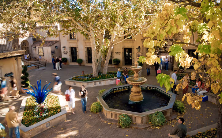 Scenic courtyard with fountain, trees, and people walking around stone buildings